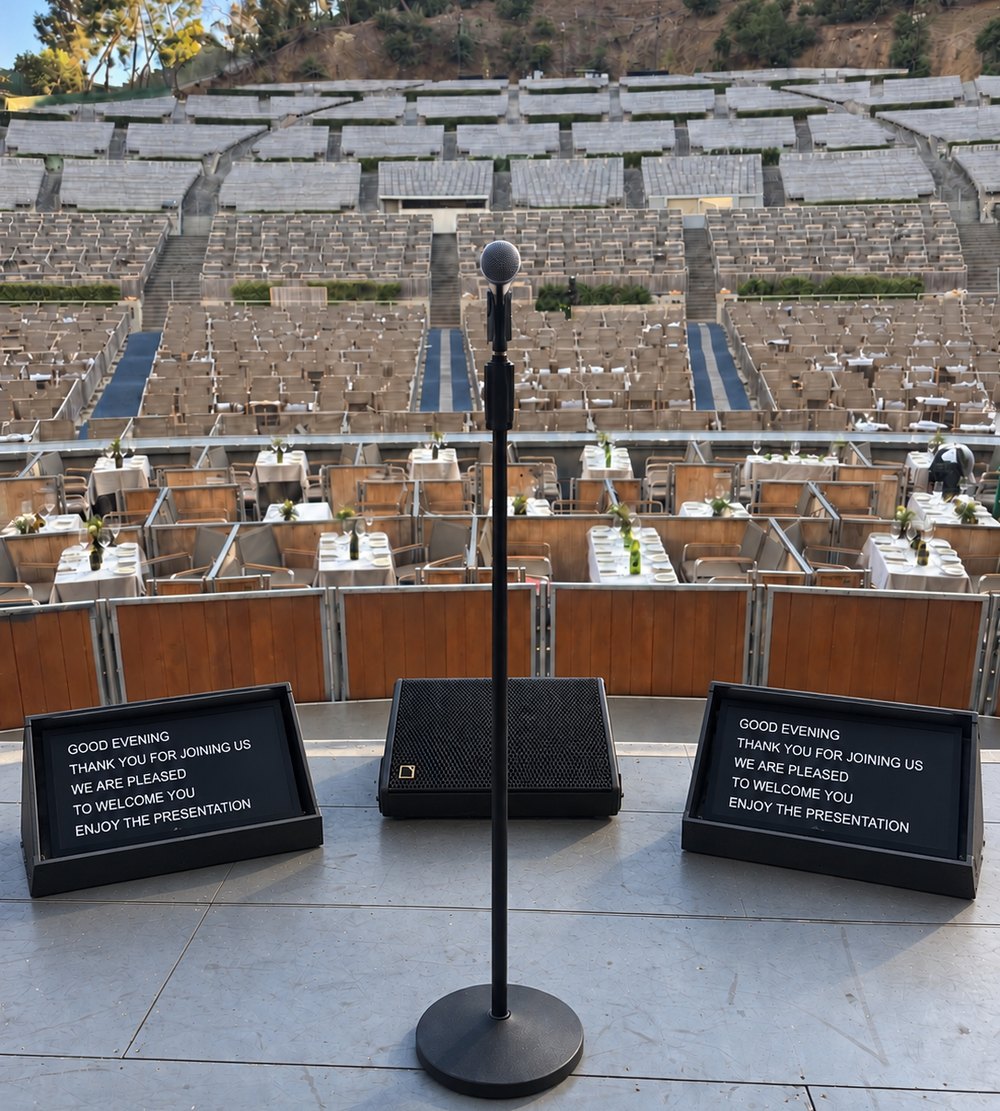 Downstage wedge monitors either side of a microphone on a Los Angeles amphitheatre stage, showing speaker copy